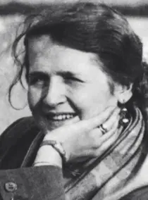 Porträt von Annedore Leber. Sie sitzt im Freien und hat ihr Kinn in die linke Hand gestützt. Sie schaut in die Ferne und lächelt.