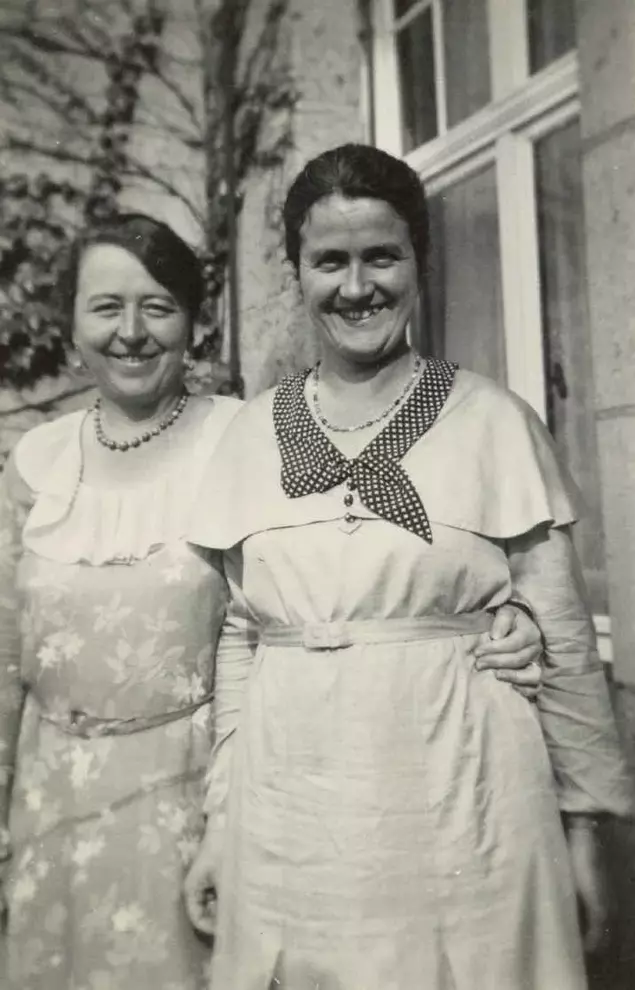 Marianne Hapig und Marianne Pünder stehen nebeneinander vor einem Haus. Sie haben die Arme umeinander gelegt und lächeln breit in die Kamera.