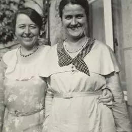 Marianne Hapig und Marianne Pünder stehen nebeneinander vor einem Haus. Sie haben die Arme umeinander gelegt und lächeln breit in die Kamera.