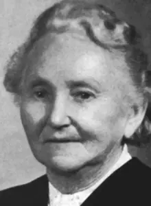 Porträt der 71-jährigen Anna Stiegler. Ihr grau-weißes Haar hat sie nach hinten hinter die Ohren gekämmt. 
