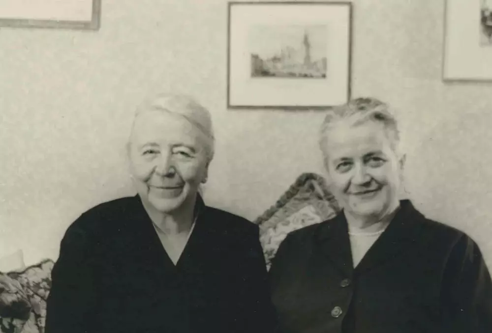 Die 61-jährige Marianne Hapig sitzt mit Marianne Pünder auf einem Sofa in einem Wohnzimmer. Sie lächeln in die Kamera.